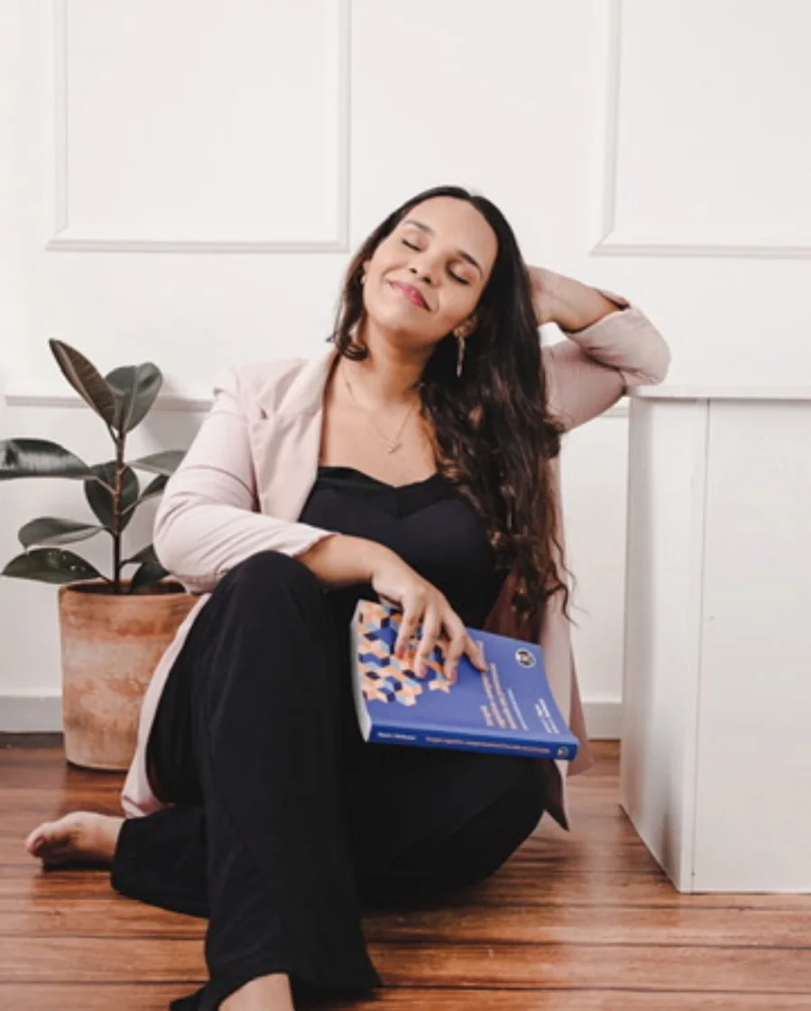 Jéssica Borowsky sentada no chão, sorrindo de olhos fechados, com um livro no colo